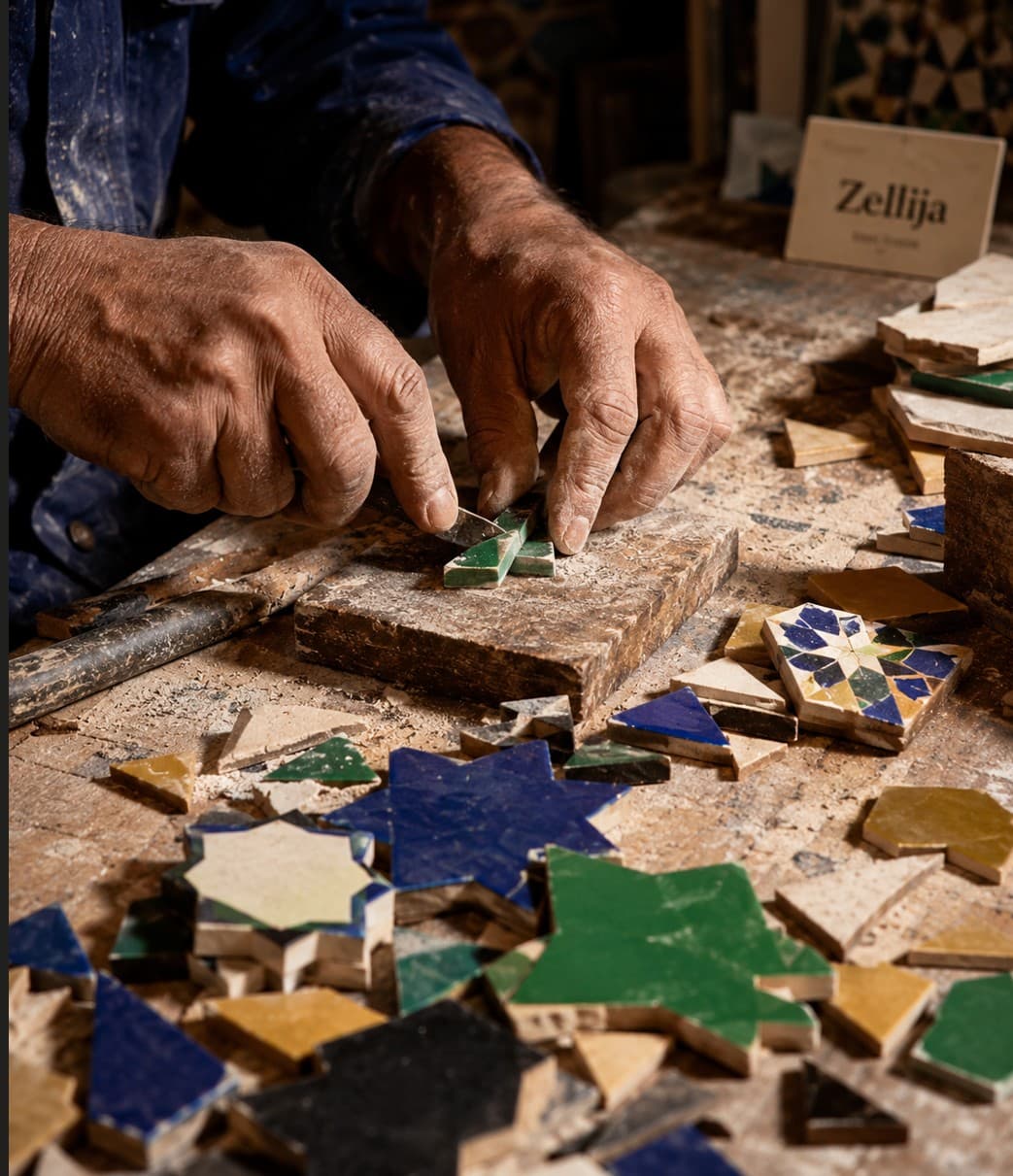 Gros plan sur les mains d'un artisan posant une pièce d'étoile verte sur un panneau de zellige dans l'atelier de Fès.