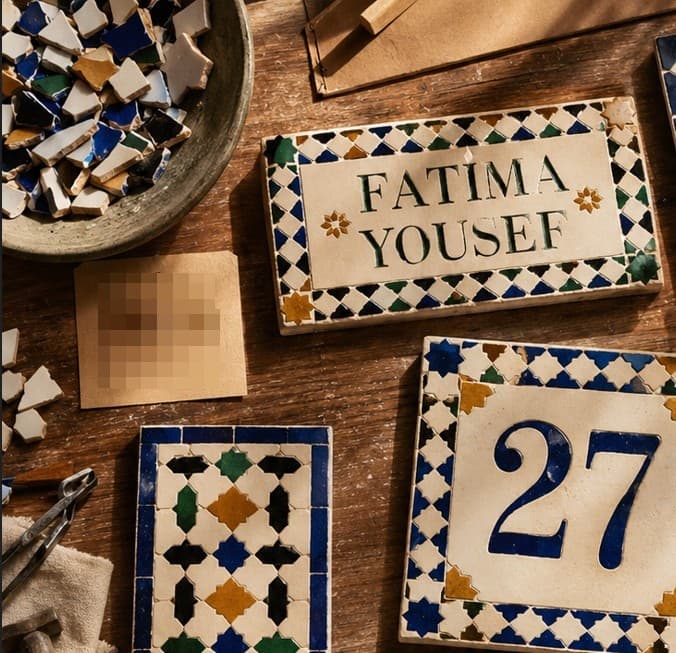 Panneau de zellige lisant Fatima Yousef avec une bordure d'étoiles géométrique en vert, bleu et safran, exposé aux côtés d'une plaque numéro 27.